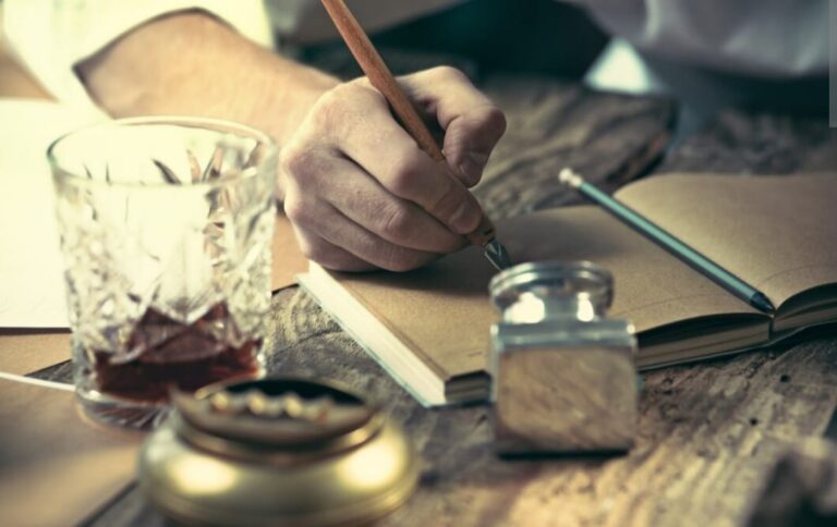 Une main écrivant au stylo plume sur un calepin posé sur une table.