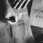 Deux mains en noir et blanc, l'une écrivant des mots en anglais avec un feutre noir.