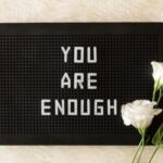 Texture de papier rectangulaire avec un rectangle noir marqué "You are enough" et trois roses dans le coin inférieur droit.